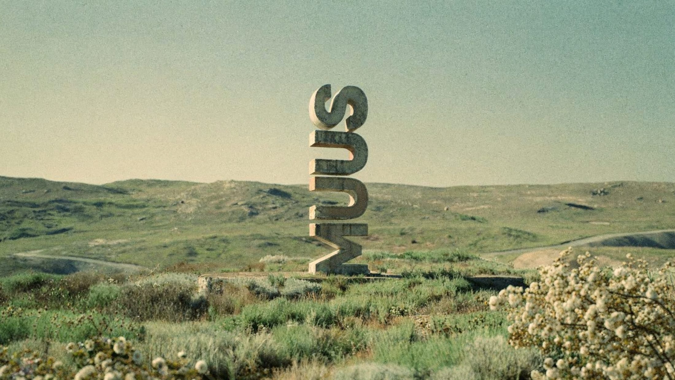 MUUS wordmark monument standing in a scrubland landscape